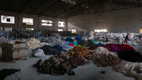 Large piles of unwanted clothes on the floor of a factory for sorting.