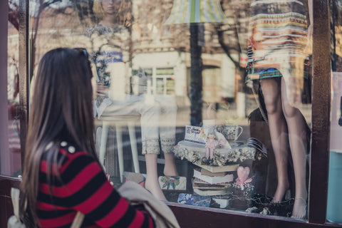 Woman looking in shop window at clothes.