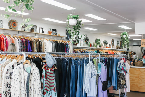 Assorted colour clothing hanging on rails in a bright and modern thrift store.