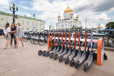 Orange and grey scooters held in a rack in the middle of a city.