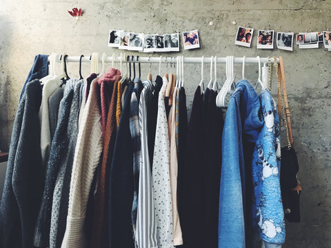 Assorted colour clothing on white rack with polariod pictures behind on concrete wall.