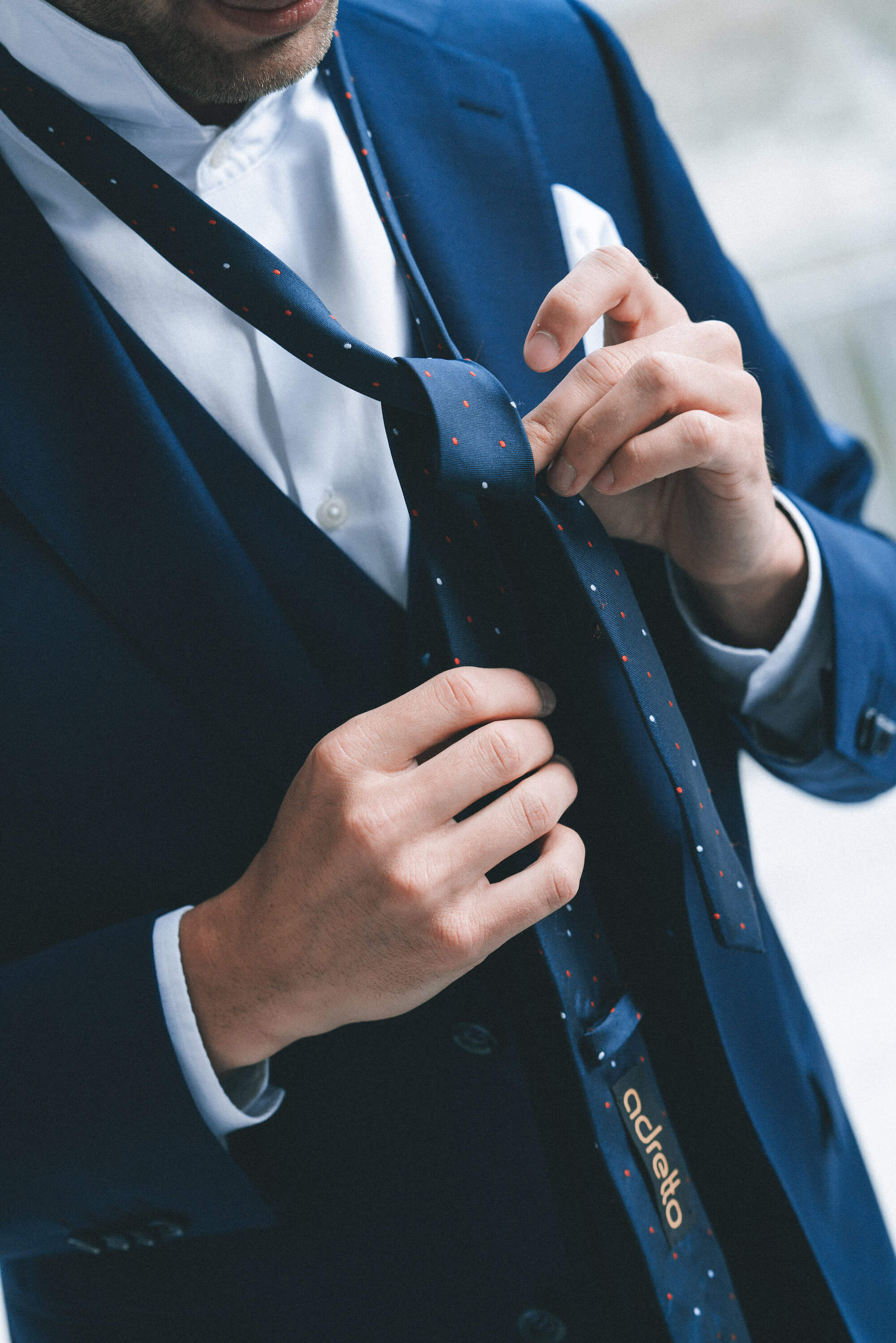 Man in blue suit tying blue tie with dots