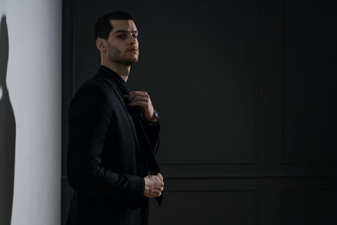 Young man in a black suit leans against the wall