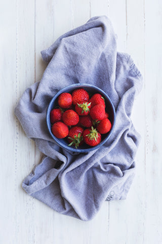 a bowl of strawberries on top of a blue tea towel