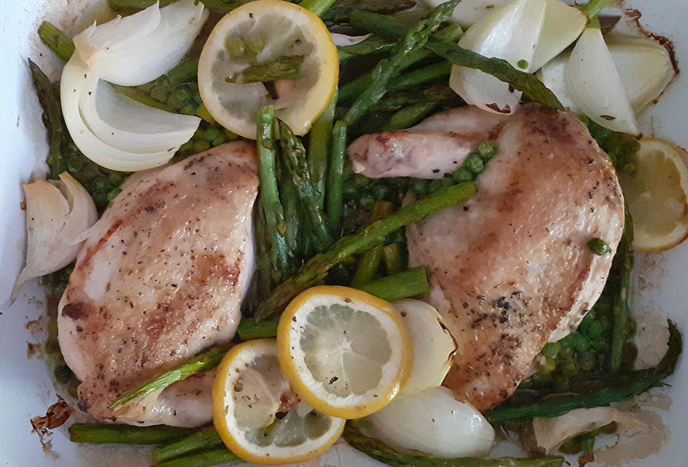 Chicken roasted in a baking tray with asparagus, peas, onions and slices of lemon
