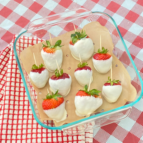 White-chocolate-dipped strawberries arranged on parchment paper in a glass baking dish