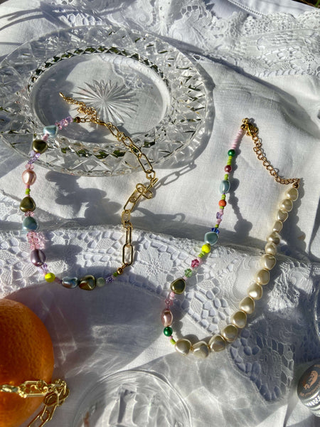 Two necklaces made from pearls, beads and gold chain on a white picnic cloth 