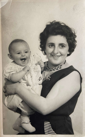 A black and white photo of a woman holding a laughing baby in the late 1950s