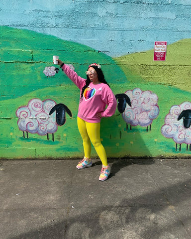 adorpheus holds aloft a chai while standing in rose city food park in Portland, Oregon wearing their pride month outfit
