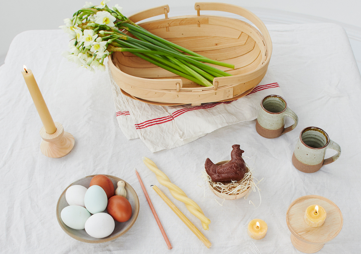 An Easter table with candles, eggs and a bunch of daffodils in a basket
