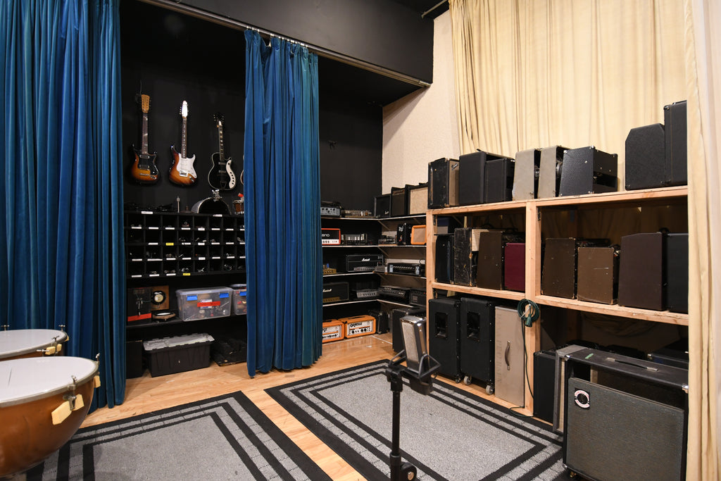 A room full of amps and a few guitars hanging on the wall. 