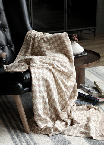 Classic Houndstooth Blanket Throw in Champagne draped over a black, leather reading chair