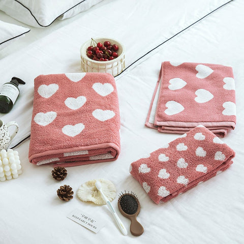 Pink Elementary Shapes Towel (with heart patterns) on white bedding with assortment of decorations such as a brush, pine cones, and candles.