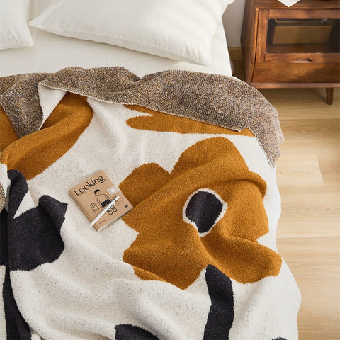 A bird's eye view shot of a white bed with a Flower Dance Blanket draped over it. It has a book on top.