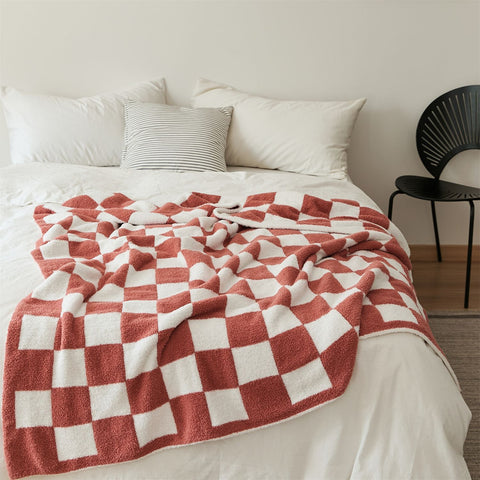 Our Retro Checkerboard Plus Blanket in Firebrick laid over a bed with white bedding sheets