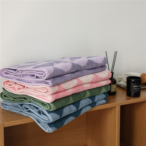 A pile of Wave Towels in different colours (Purple, Light Coral, Seagreen and Steel Blue) onto of a brown, wooden shelf.