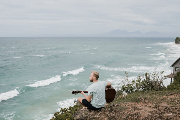 Mann sitzt mit Guitarre am Meer