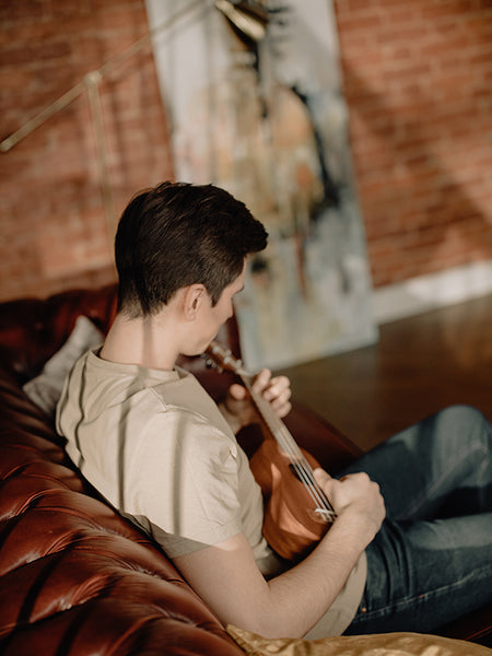 Mann sitzt mit dem Rücken zum Betrachter auf dem Sofa und spielt Ukulele