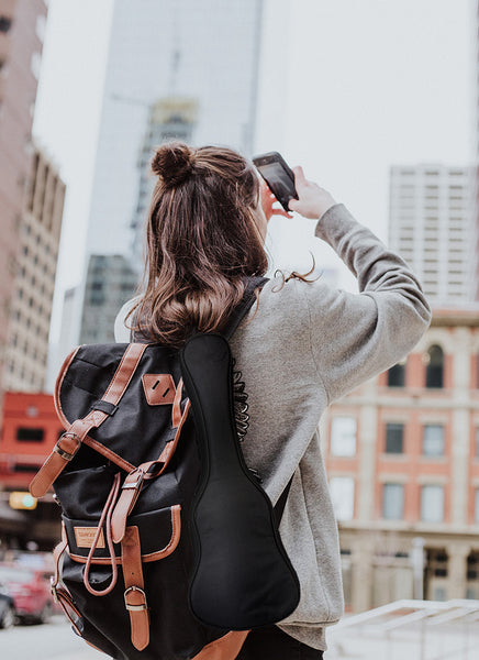 Junge Frau mit Rucksack und Ukulele fotografiert Hochhäuser 