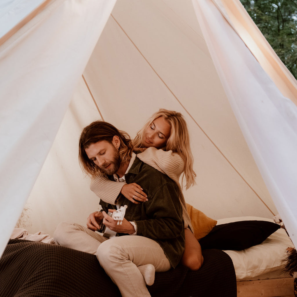 Frau umarmt Mann der Ukulele spielt in einem weißen Zelt