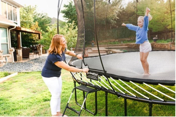 A mother zipping a trampoline closed while her daughter jumps.