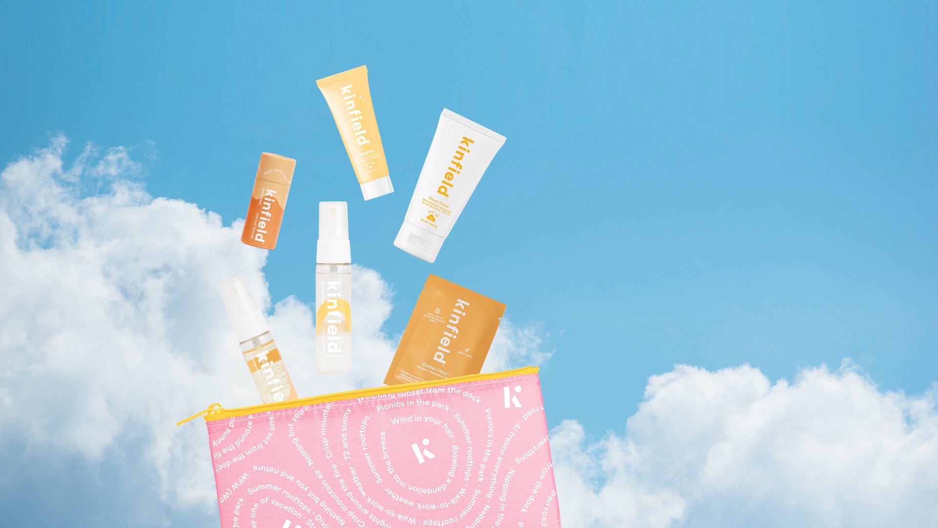 Travel sizes of Kinfield bestsellers and a pink Kinfield bag scattered across a blue sky with fluffy white clouds.