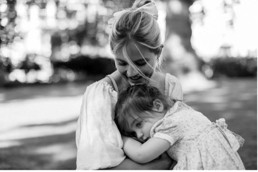 Black and white photo of Tabitha and her toddler in an embrace, outside on a sunny day.