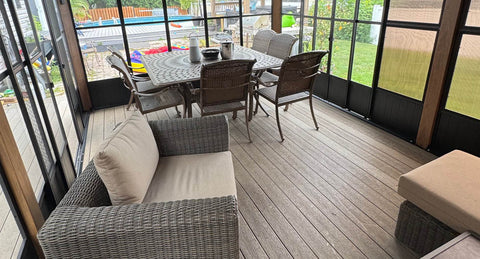 A sunroom with large windows and screens features a wooden-style floor and patio furniture.