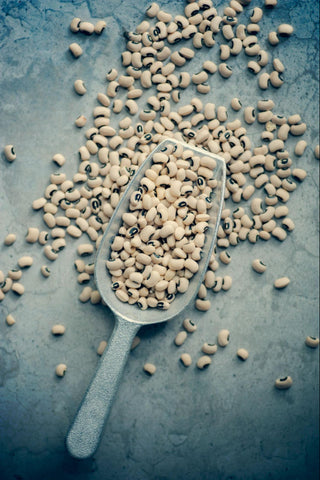 An overflowing scoop full of uncooked black-eyed peas.