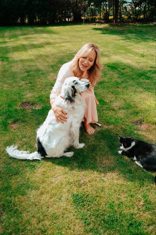 A woman smiles at a calm dog and cat on a lawn.