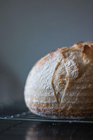 A deliciously fresh loaf of sourdough bread rests on a cooling rack.