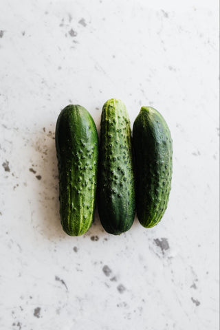 Three green ripe cucumbers on a white marble surface.