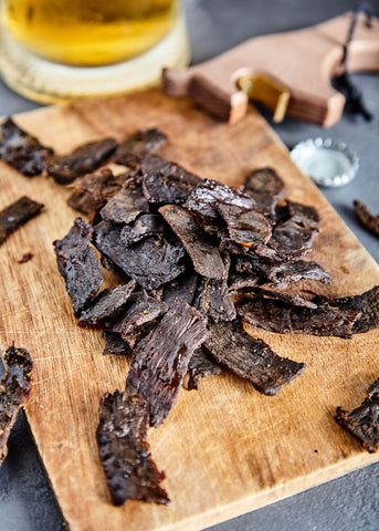 A cutting board covered in slices of beef jerky.