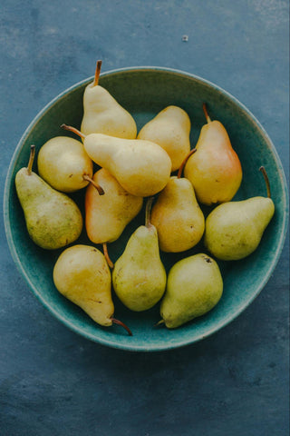 A turquoise blue bowl full of fresh pale green and yellow-skinned pears.