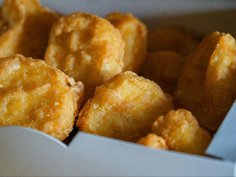 Several golden brown chicken nuggets in a white box.