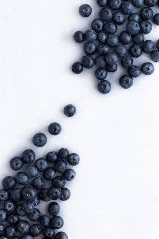 Many blueberries scattered on a white surface.