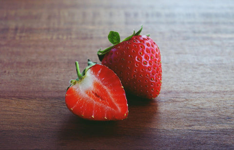 A strawberry and a halved strawberry sit on a wooden table.