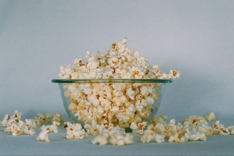 A glass bowl with popcorn spilling over onto the surface beneath it.