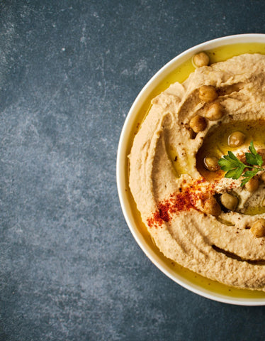 A bowl of hummus with chickpea, paprika, and parsley garnish.