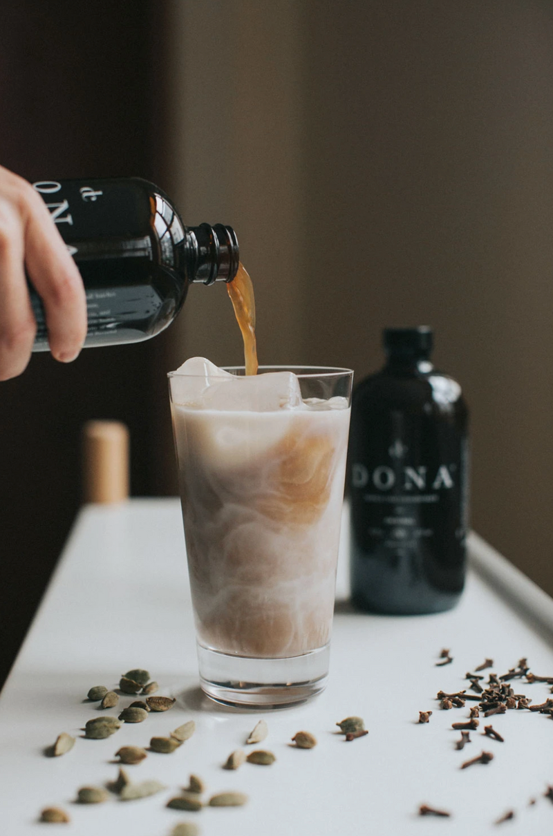 Someone pouring out a container of Dona Masala Chai Concentrate into a glass