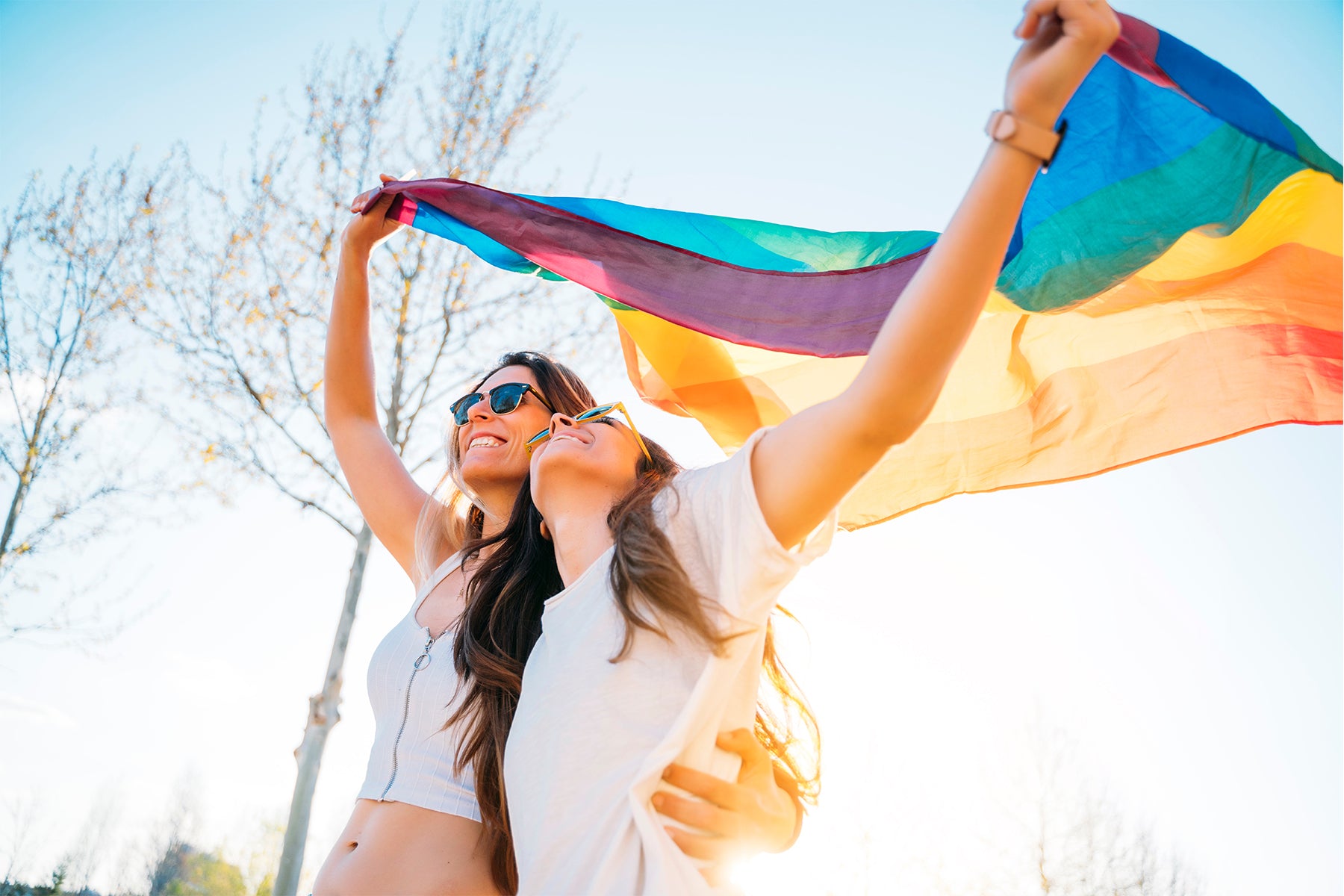Two Lesbian Women Holding Up a Rainbow Pride Flag | Rainbow & Co