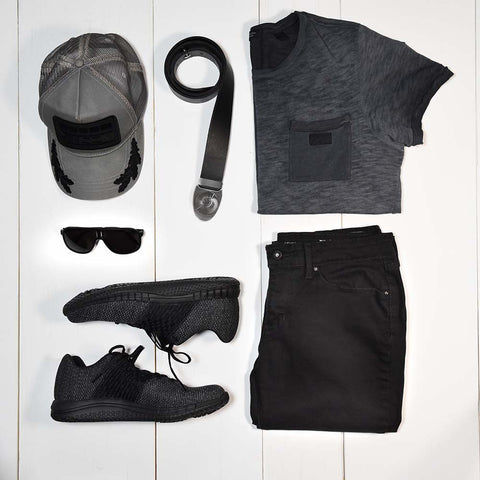 teen style flat lay. Outfit items include black jeans, marled grey t-shirt, sunglasses, stylish trucker hat, black sneakers, and a black and silver belt