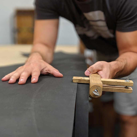 man's hands cutting a cowhide of full-grain leather using a strap cutter hand tool. these will be made into men's leather belts.