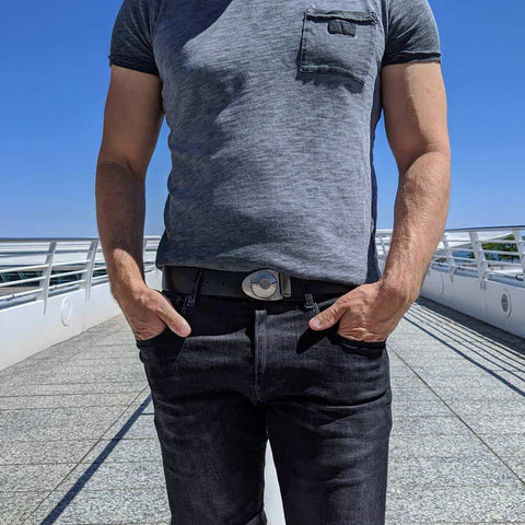 Man wearing black leather belt with silver belt buckle on dark jeans by a modern art museum