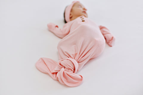 Newborn wearing a light pink knotted gown and headband