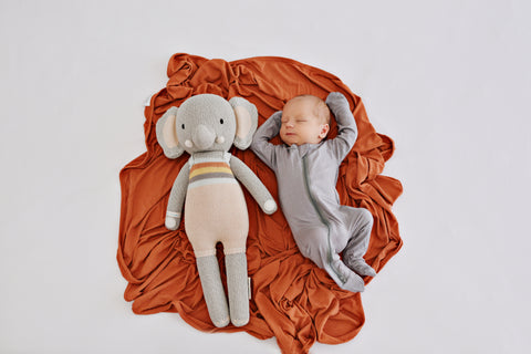 Newborn wearing a gray baby romper next to a stuffed animal
