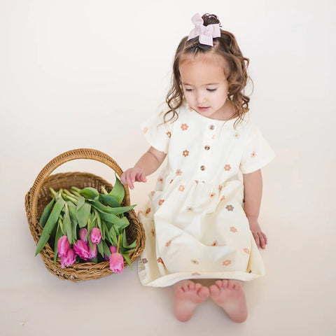 Little girl in a twirl dress sitting down next to a basket of flowers