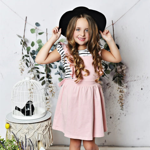 Little girl wearing a black hat and pink pinafore dress