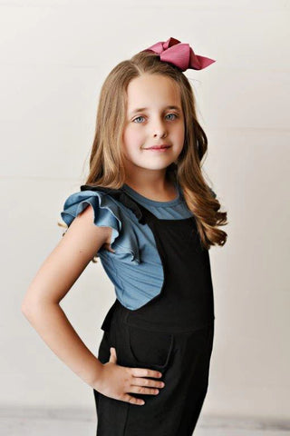 Girl wearing a blue ruffle tee and black overalls