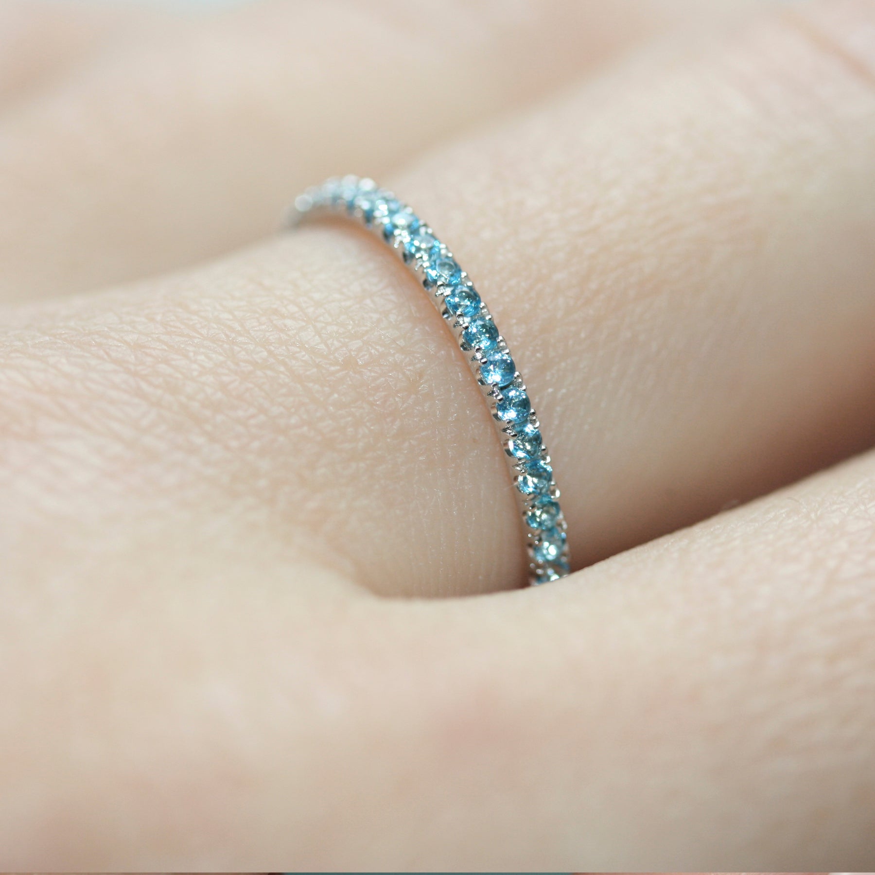 Closeup of a blue Topaz eternity ring in platinum on a hand.